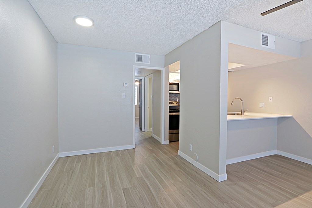 a bedroom with a desk and a kitchen in the background