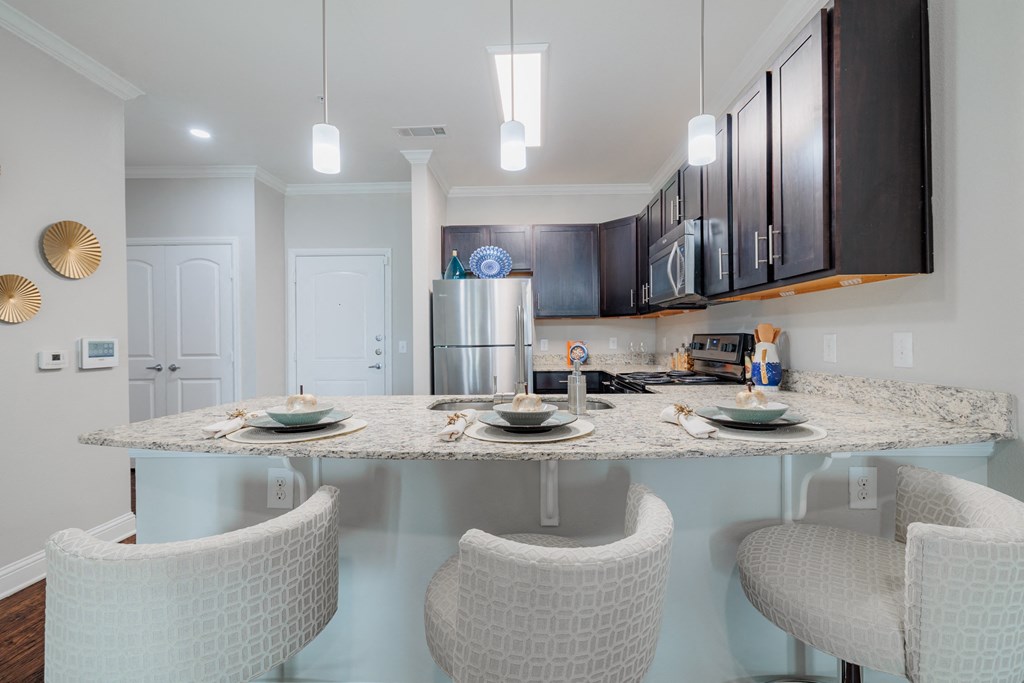 a kitchen with a granite counter top and a bar with three chairs