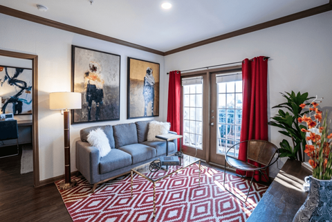 A living room with a grey couch, a red rug, and a painting on the wall.