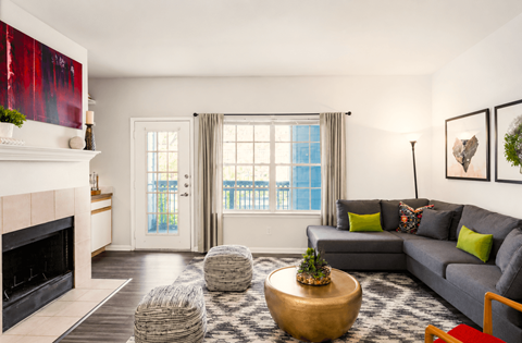 A living room with a grey couch, a fireplace, and a large window.