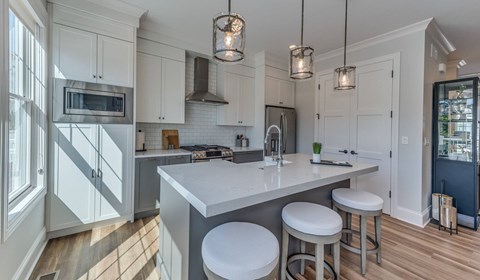 A kitchen with white cabinets and a large island with three stools.