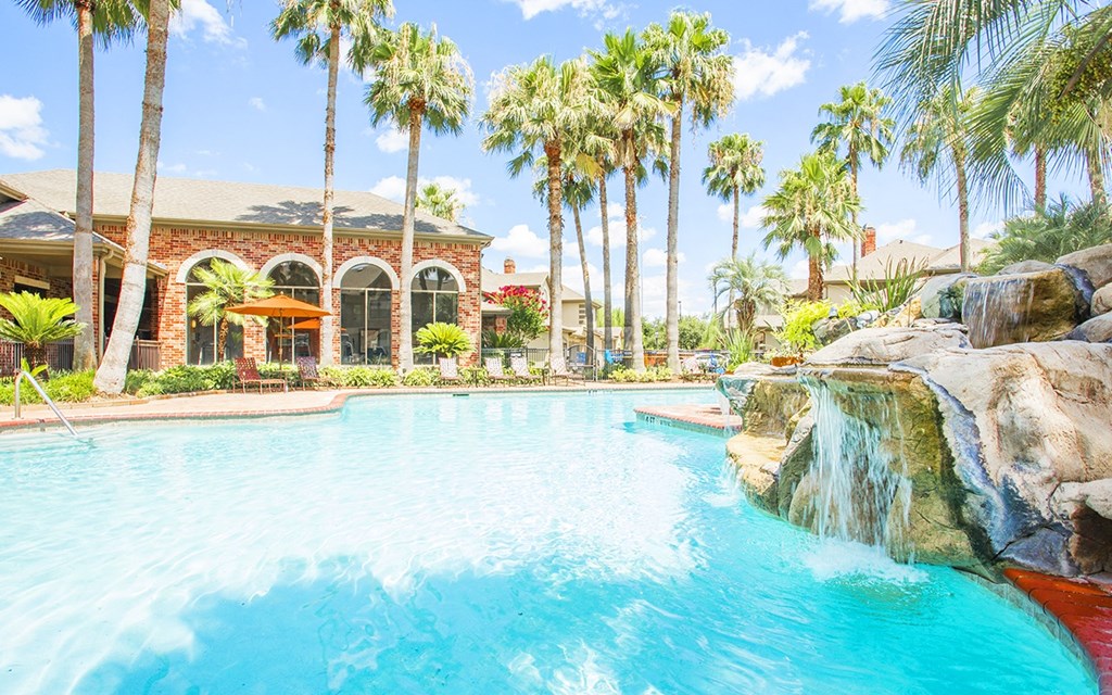 a large swimming pool with a waterfall and palm trees