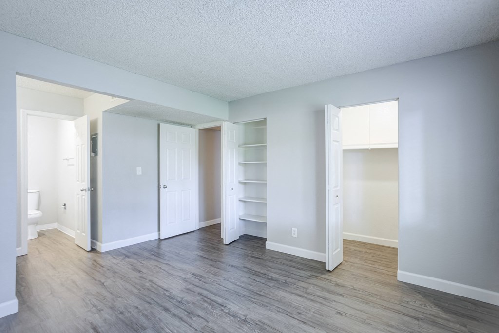 A room with white walls and wood flooring with a doorway leading to another room.