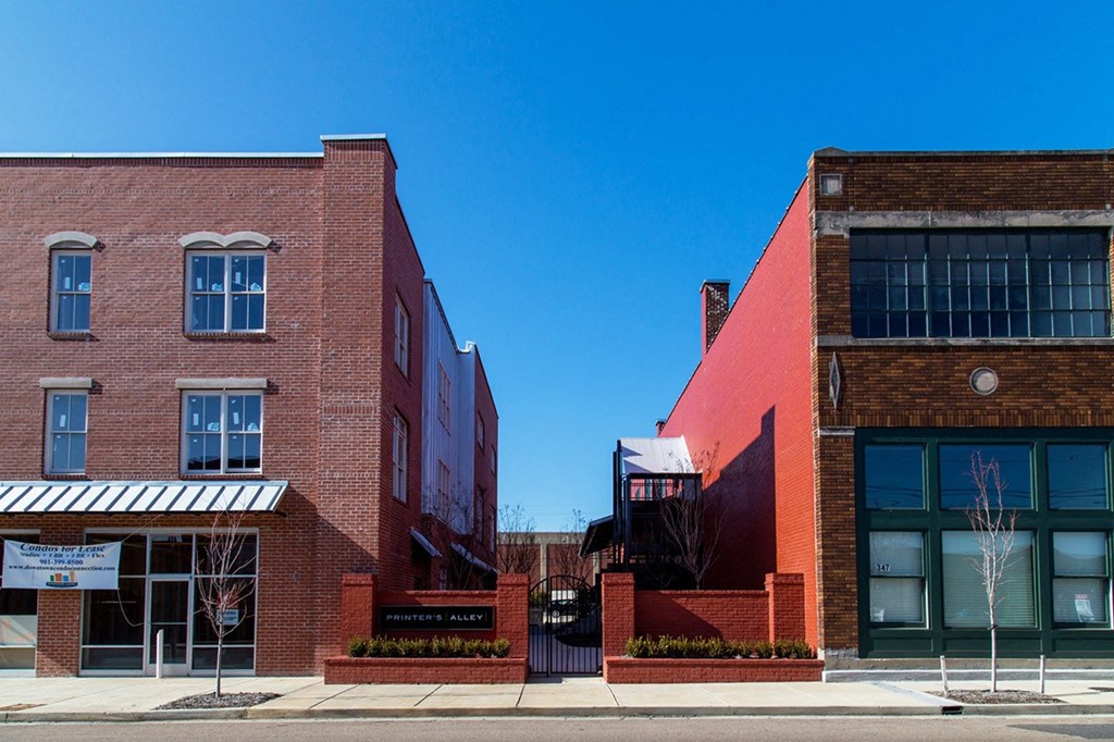 a pair of red brick apartment buildings on a street with a blue sky in the background