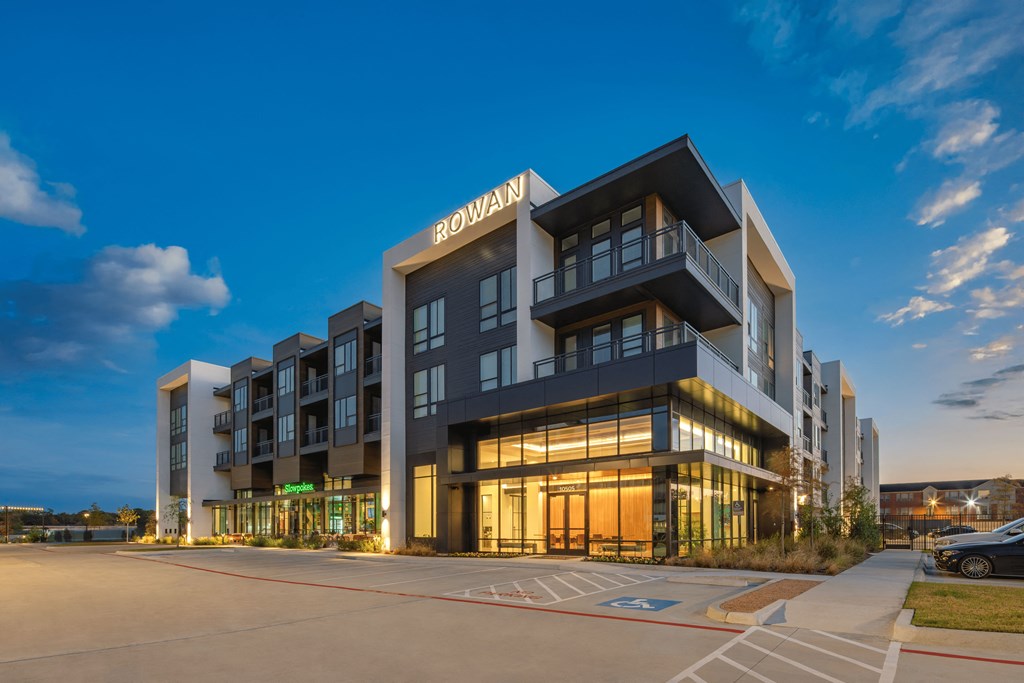 A modern multi-story building named "Rowan" is illuminated at dusk.