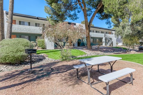 A picnic table and bench are in the foreground of a courtyard with a building in the background.