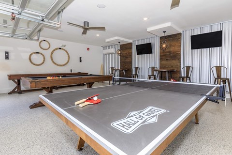 A ping pong table with the words "Hall of Fame" on it is in the middle of a room with a wooden bench and a TV.