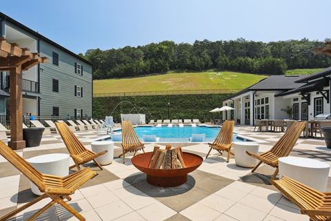 a pool with a fire pit and lounge chairs in front of a building with a grassy