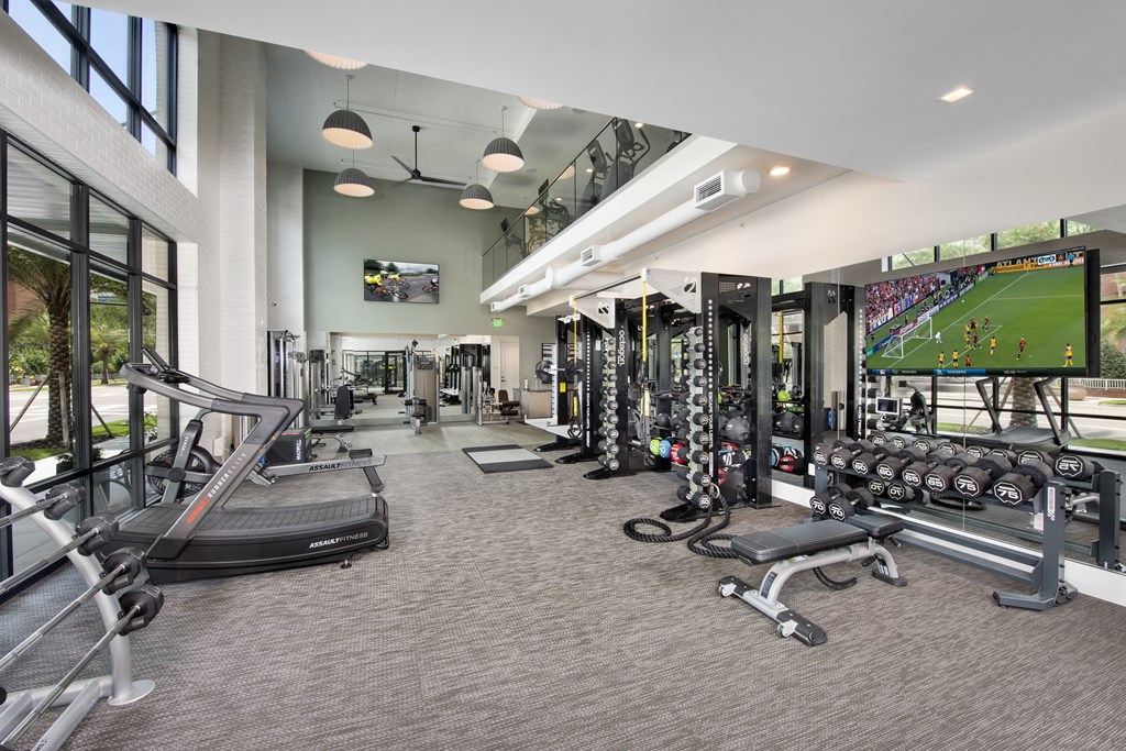 a gym with cardio machines and weights and a large tv