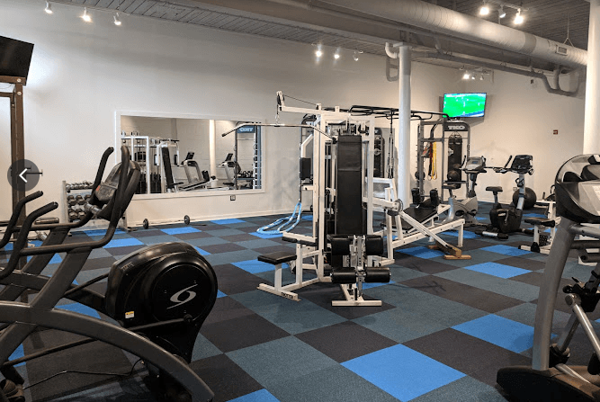 A gym with a variety of equipment including a squat rack, a bench press, and a leg press machine.