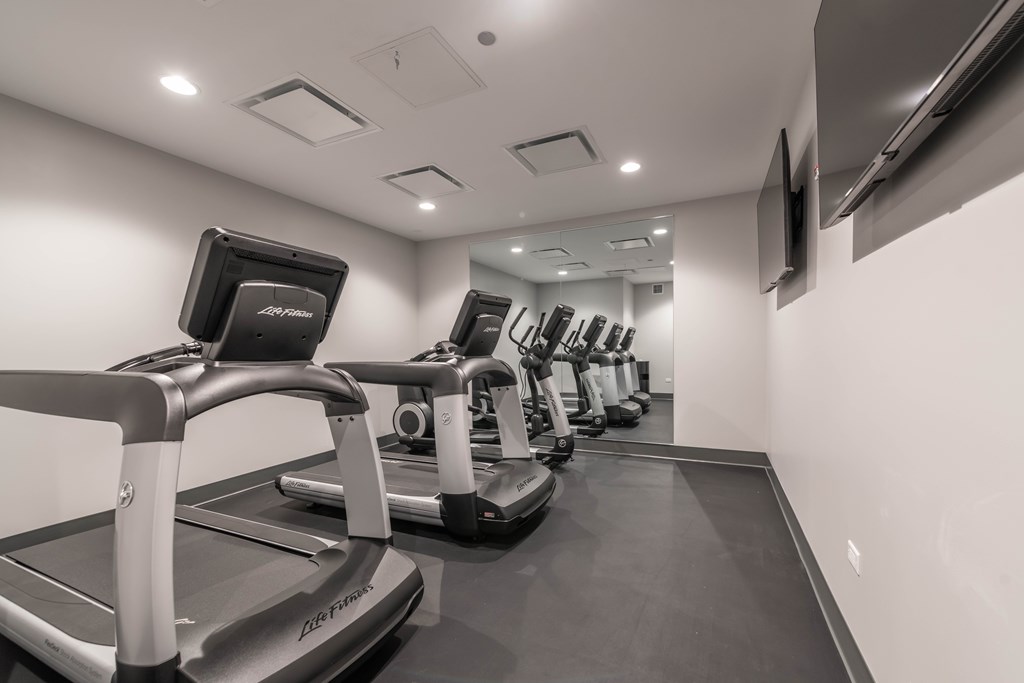 A treadmill in a gym with a monitor on the side.