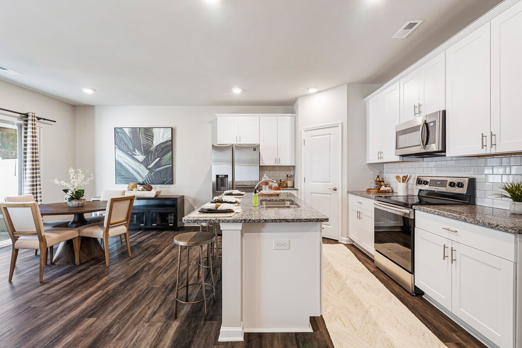 A modern kitchen with white cabinets and a wooden floor.