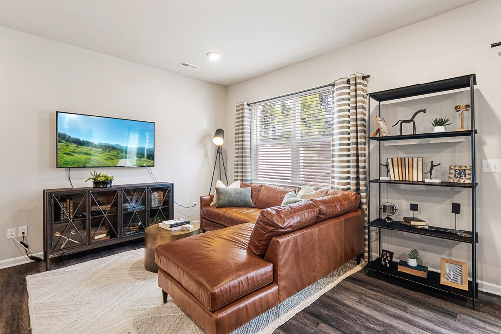 A living room with a brown leather couch and a television mounted on the wall.
