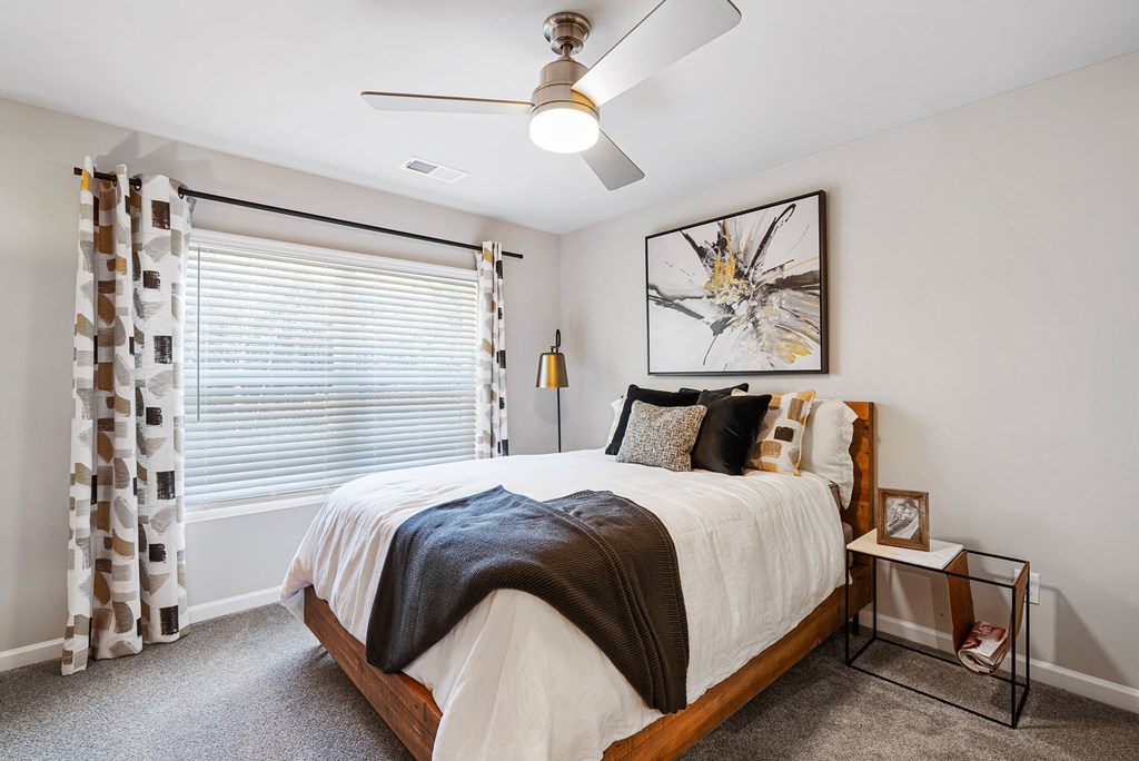A bedroom with a bed, a ceiling fan, and a window with curtains.