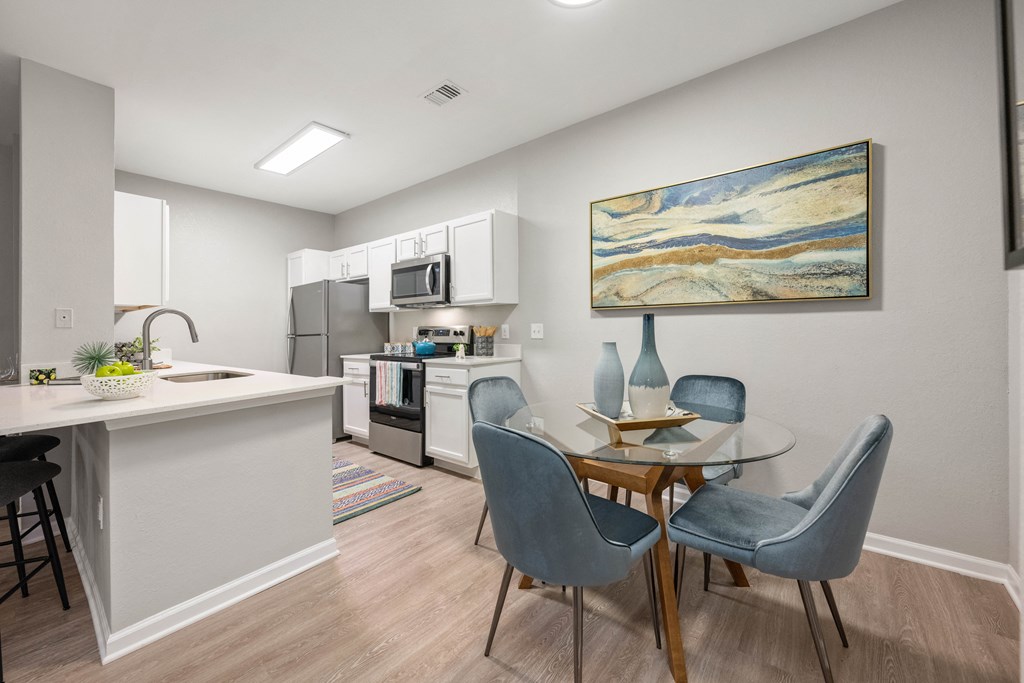 a dining room with a table and chairs and a kitchen with a sink and microwave