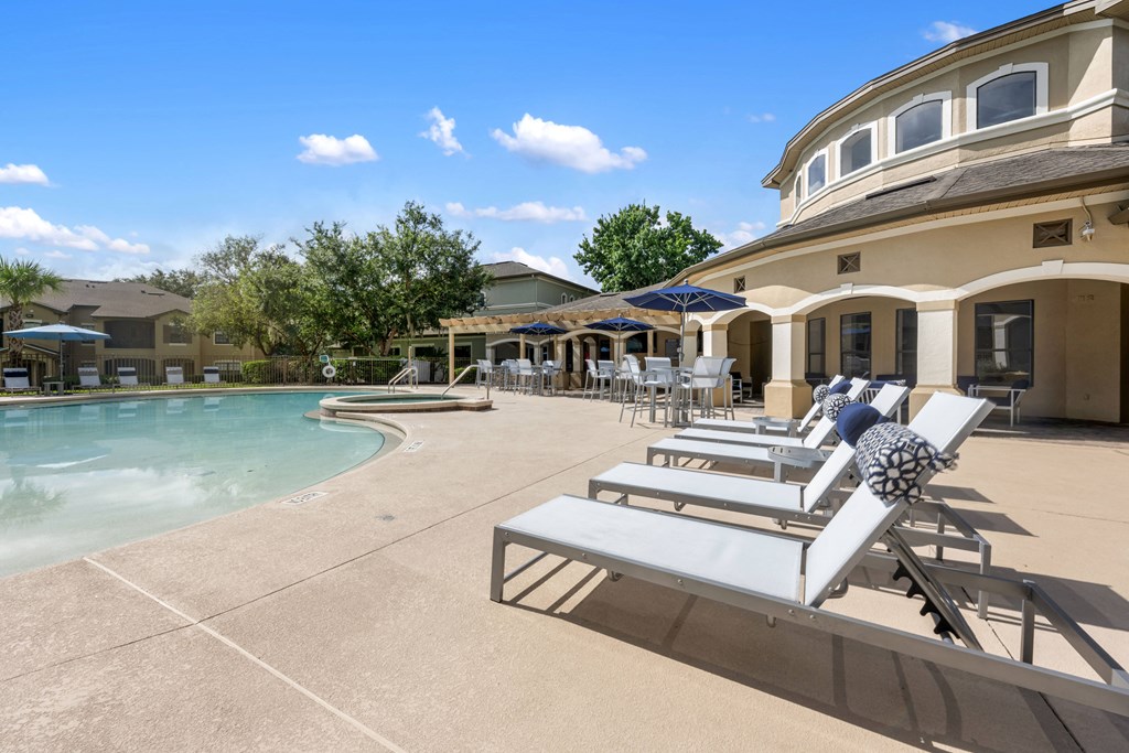 a pool and patio with chairs and umbrellas in front of a house