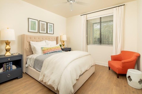 A bedroom with a large bed, a chair, and a nightstand with a lamp.
