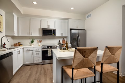 A kitchen with a white counter top and brown chairs.
