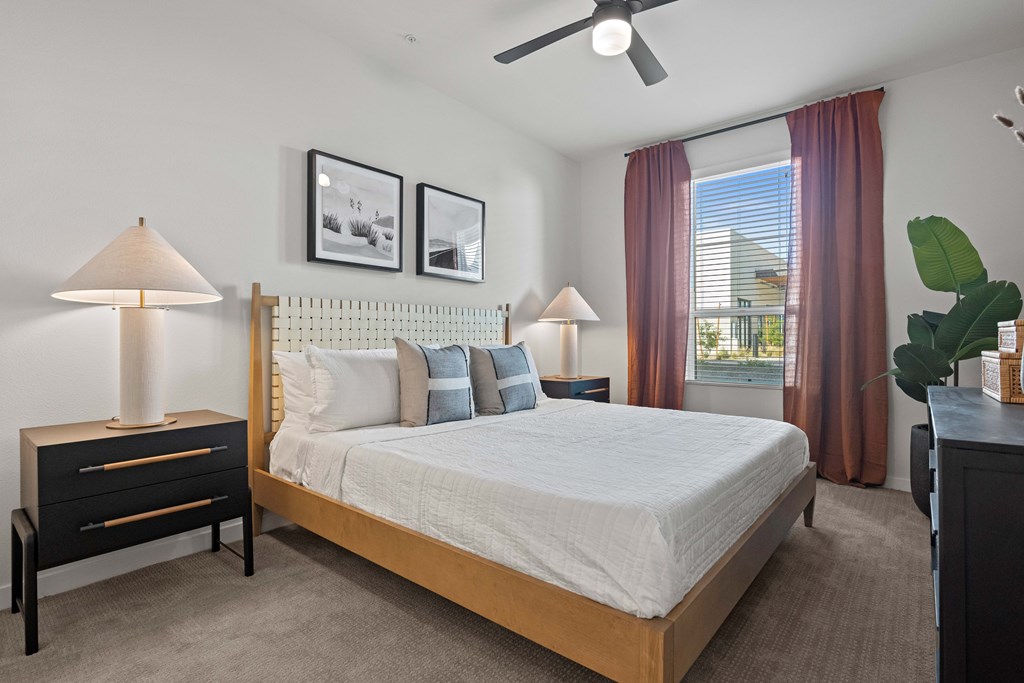 A bedroom with a large bed, a nightstand with a lamp, and pictures on the wall.