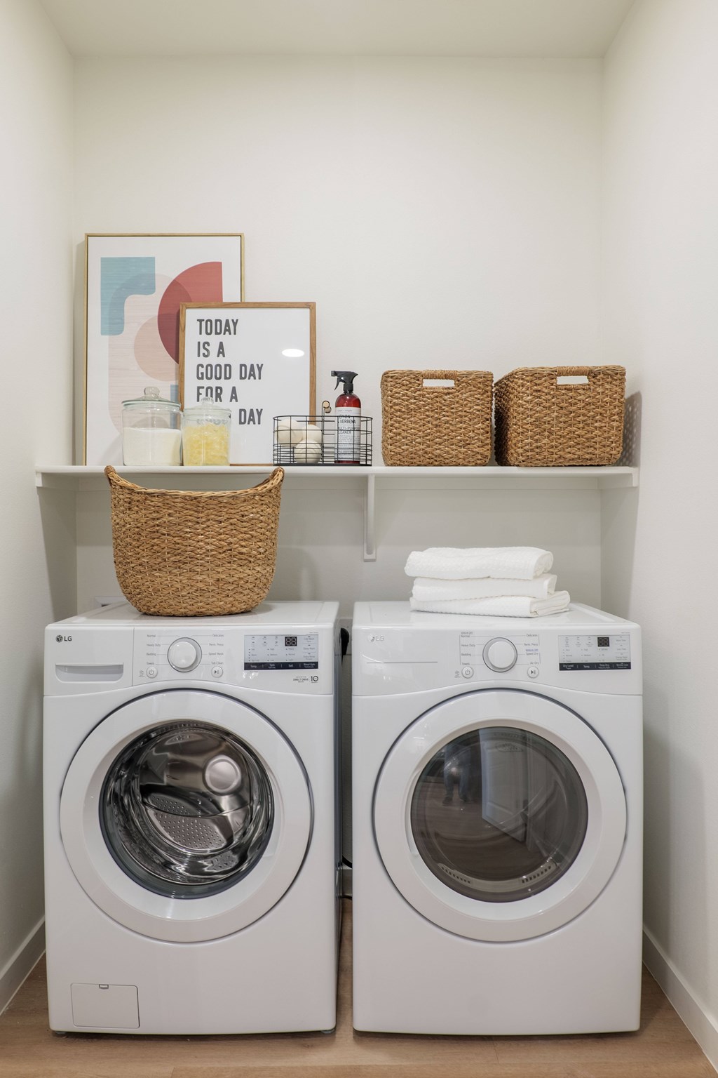 Two washing machines are in a laundry room with a basket on top of the shelf.