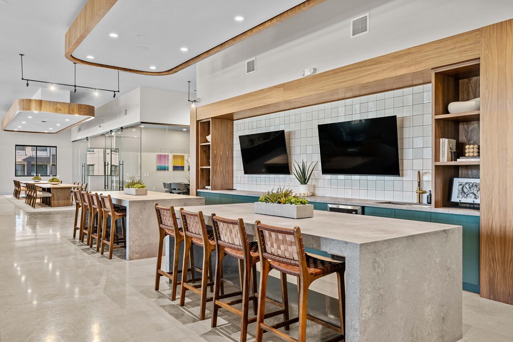 A modern kitchen with a long bar and wooden chairs.