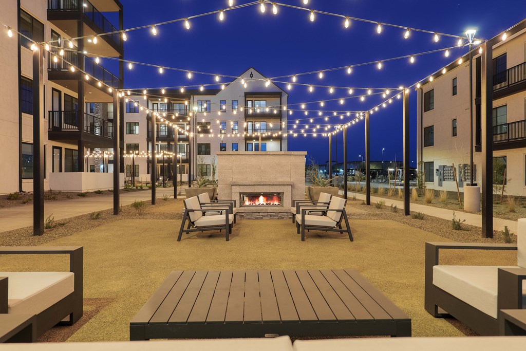 A patio with a fireplace and chairs under string lights.