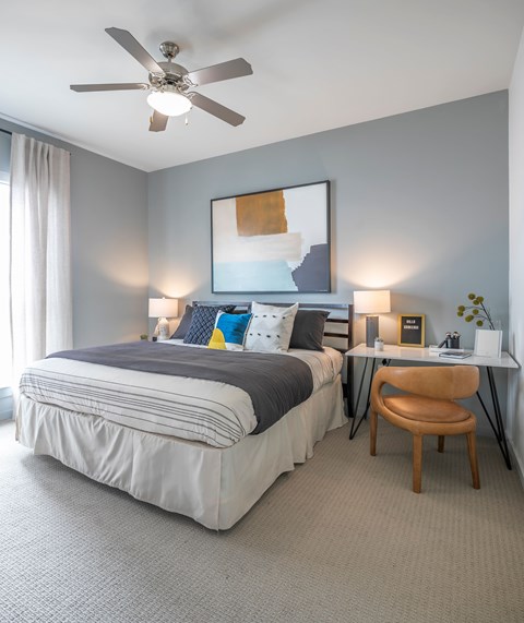 A bedroom with a bed, desk, chair, and a ceiling fan.