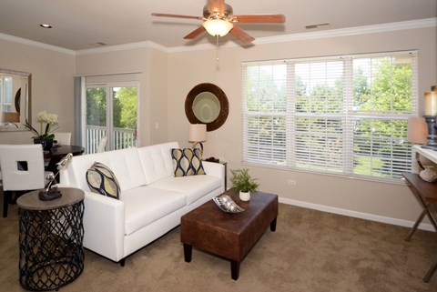 A living room with a white couch, a brown ottoman, and a ceiling fan.