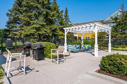 A white pergola is in the middle of a patio with chairs and a table.