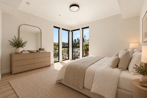 A bedroom with a large bed, a dresser, and a view of the outdoors through the windows.