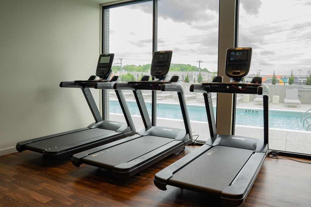 a row of treadmills in a gym with a view of a swimming pool