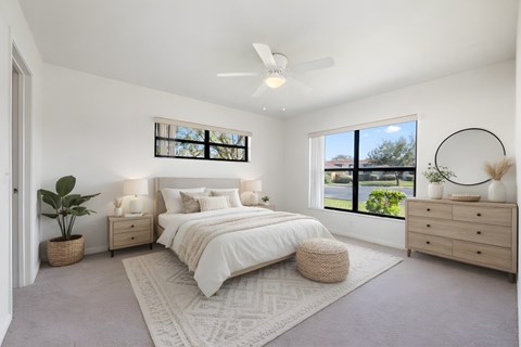 A bedroom with a large bed, a ceiling fan, and a window with a view of the outdoors.