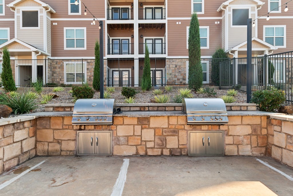 A wall of apartment buildings with a stone wall and grills in front.