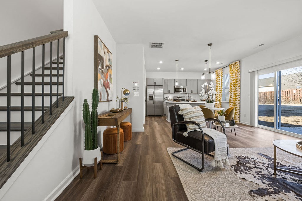 A modern living room with a staircase on the left and a dining area in the background.