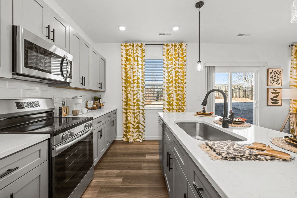 A modern kitchen with a stainless steel oven and a window with yellow curtains.