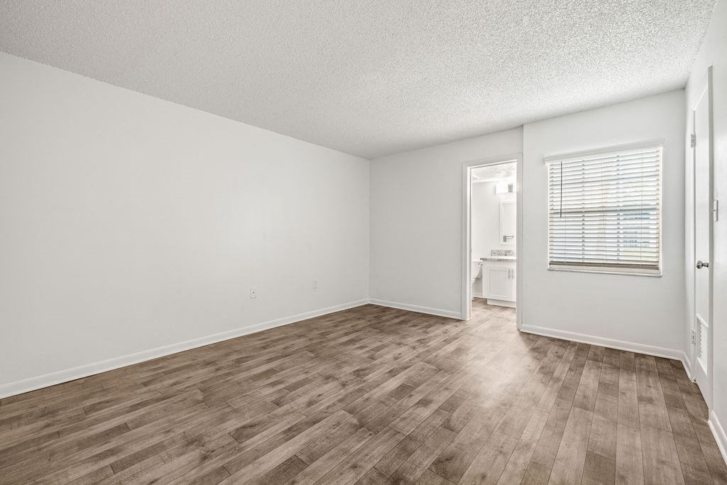 an empty living room with wood flooring and a door to a bathroom