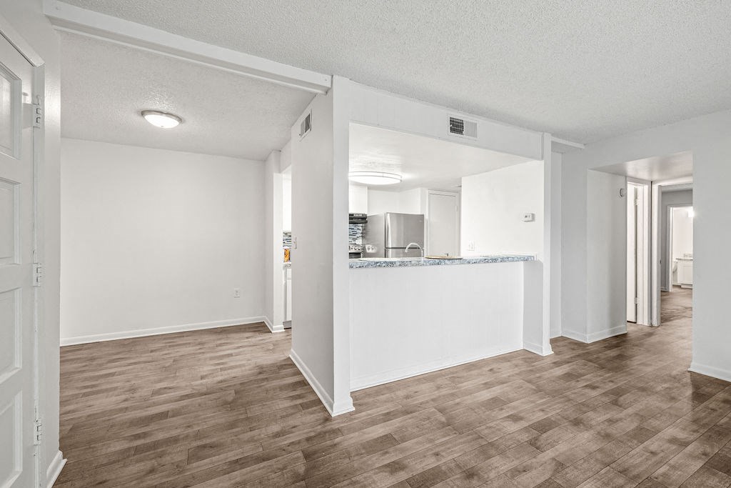 an empty living room with a kitchen in the background