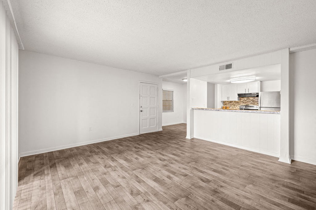 an empty living room and kitchen with wood flooring