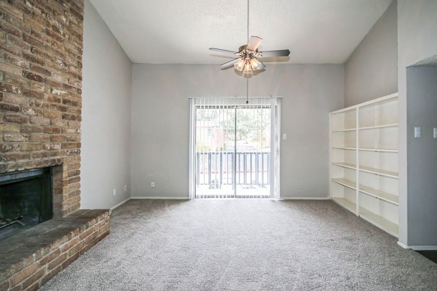 an empty living room with a brick fireplace and a ceiling fan