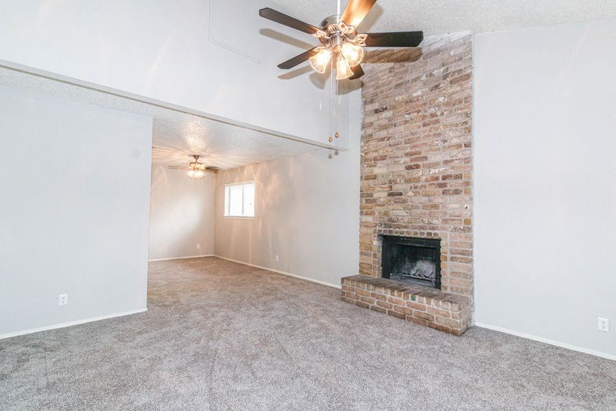 an empty living room with a brick fireplace and a ceiling fan