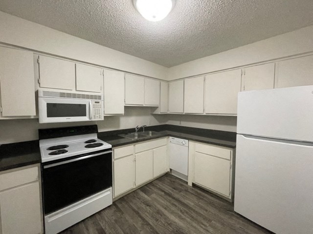 a kitchen with white cabinets and black counter tops and white appliances