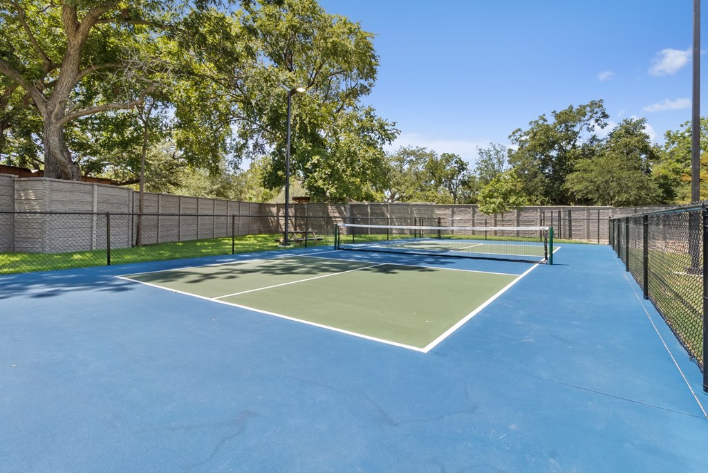 A tennis court surrounded by a fence and trees.