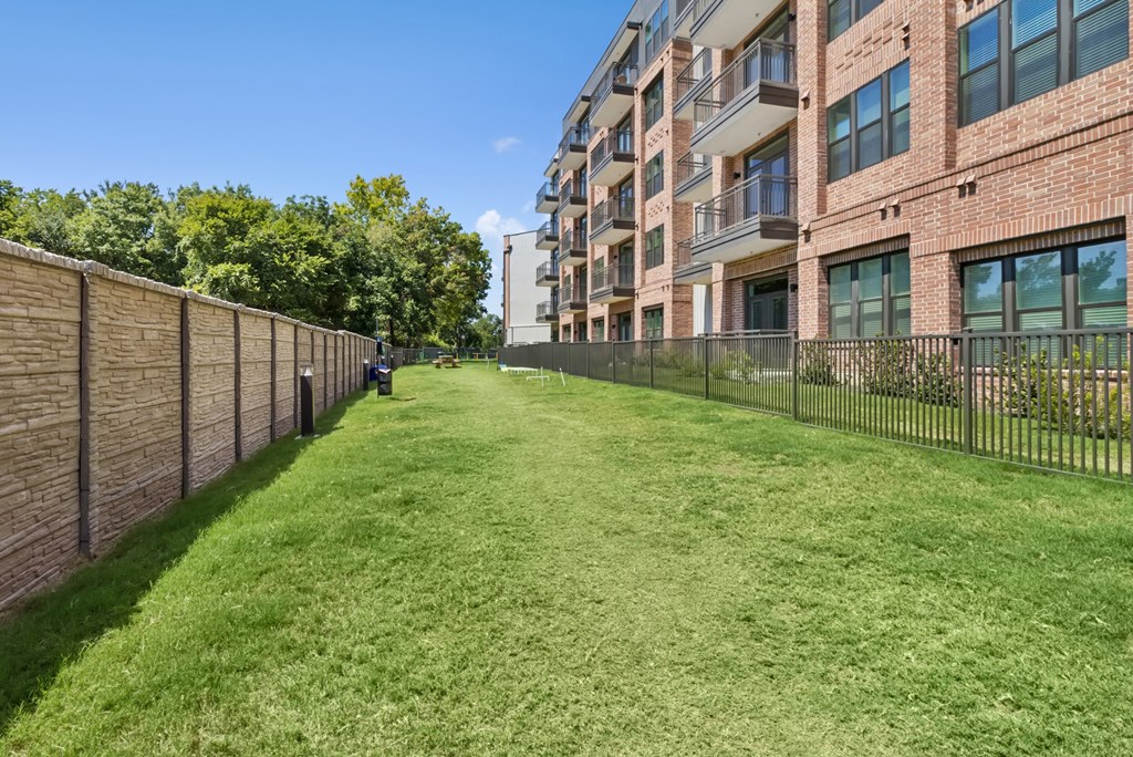 A grassy area in front of a brick building with a fence.