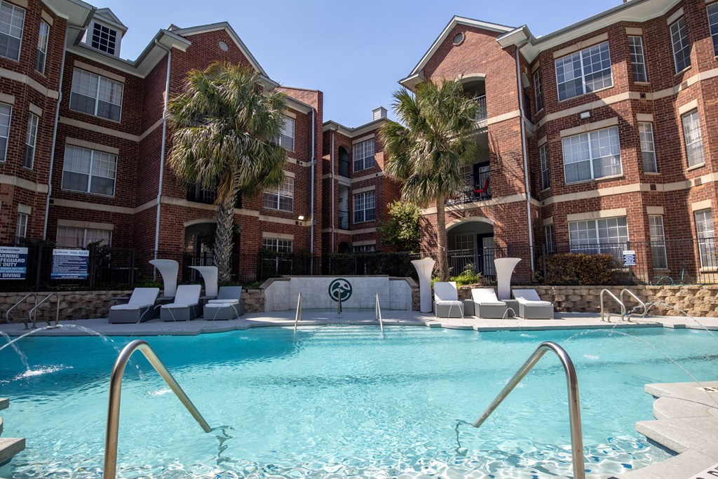 A swimming pool in front of a red brick building with palm trees.