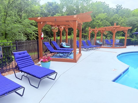 A poolside area with blue lounge chairs and a wooden pergola.