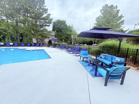 A pool with a blue umbrella and chairs.