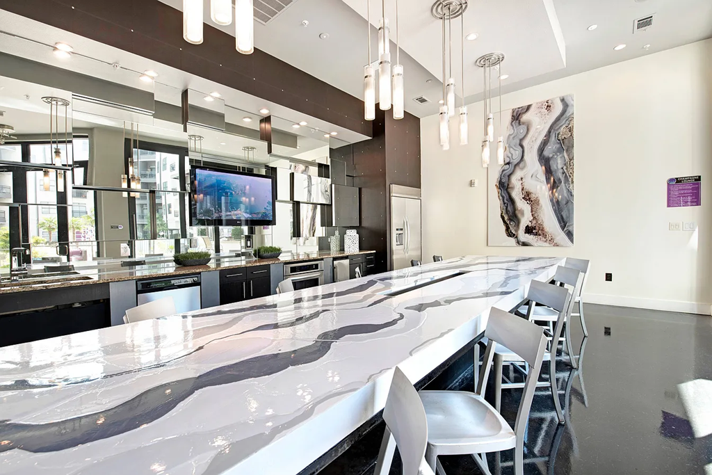 A long white marble bar with white chairs and a TV on the wall.