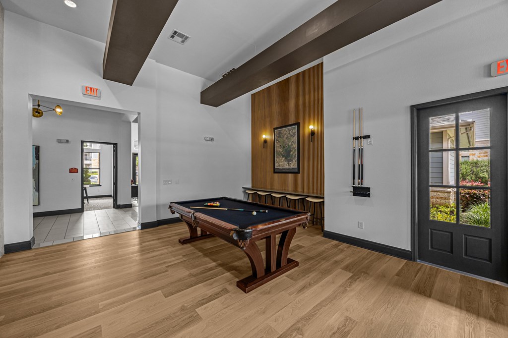 A pool table is in the middle of a room with a door to the left and a window to the right.
