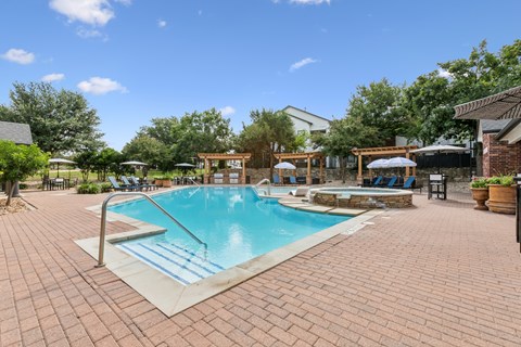 A pool surrounded by a brick patio with a blue sky in the background.