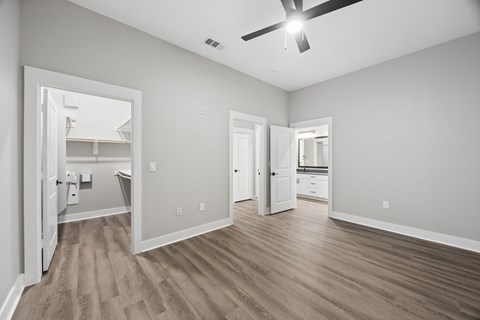 A spacious room with a ceiling fan and light, hardwood floors, and a view into another room through an open door.
